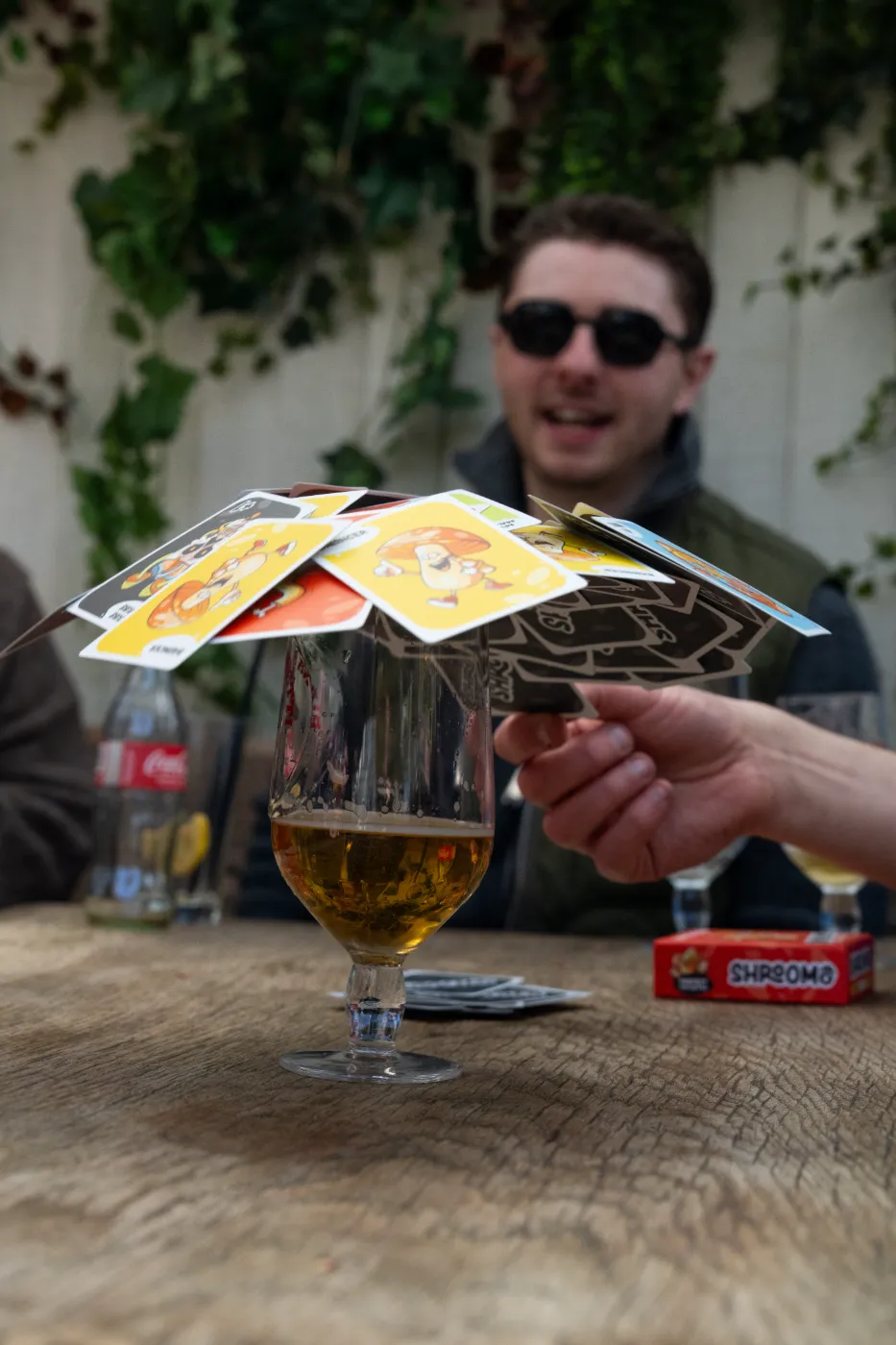 Friends playing Shroomo, stacking cards on a glass at a house party